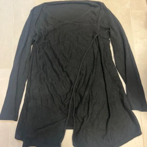 Svart omlottkofta med lång ärm - Svart omlottkofta med lång ärm och enkel design. Koftan har en mjuk och tunn stickad känsla, perfekt att slänga över en topp. Snygg omlott-detalj framtill som ger en avslappnad men stilren look.