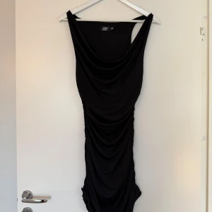 Svart draperad klänning Tiger Mist XS - Supersnygg svart kortklänning från Tiger Mist i figurnära modell med draperad effekt framtill och breda axelband. Klänningen är använd en gång och i mycket bra skick! Säljs för att den ej kommer till användning 