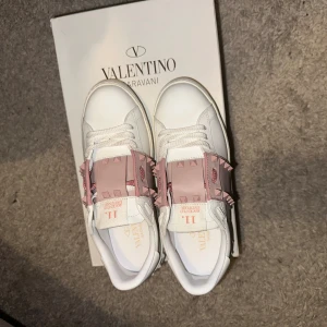 Valentino Rockstud sneakers vit/rosa - Snygga Valentino Rockstud sneakers i vitt skinn med ljusrosa detaljer och ikoniska nitar över vristen. Skorna har rund tå, platt sula och vita snören. Perfekta för dig som vill sticka ut med en lyxig och trendig look. Jag säljer nu dessa skor eftersom de ej kommer till användning och är lite för stora för mig. De är storlek 38