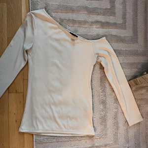 Offshoulder ljusbeige långärmad topp - Säljer en stilren offshoulder topp i ljusbeige med lång ärm. Toppen har en smickrande, tight passform och är tillverkad i mjuk ribbad bomull. Perfekt för dig som gillar minimalistisk och trendig stil.