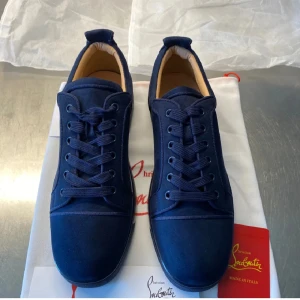 Mörkblå sneakers från Christian Louboutin - Snygga mörkblå sneakers från Christian Louboutin med klassisk röd sula. Skorna har rund tå, snörning och är tillverkade i mocka med diskret broderad logga på hälen. Insidan är ljusbeige och sulan är i gummi. Perfekta för dig som vill sticka ut med stil.