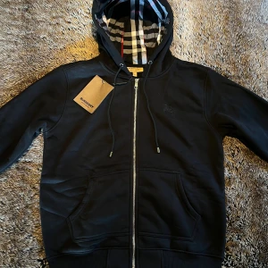 Burberry Hoodie - Säljer en helt ny svart Hoodie från Burberry i Storlek L men kan funka för M okså, riktigt skönt och varmt material. Original lapparna medföljer vid köp och vid frågor eller funderingar är det bara att höra av dig ☀️