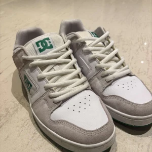 DC Shoes vita och grå sneakers i storlek 45 passar 44!  - Säljer ett par DC Shoes sneakers i vitt och ljusgrått med gröna detaljer och logga. Skorna har snörning, rund tå och platt sula med grön undersida. Ovandelen är i mocka och textil, perfekt för dig som gillar skate- eller streetstil! Använda väl men fortfarande i bra skick! 
