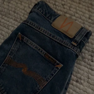 Marinblå Nudie Jeans 30/32 (Oanvända)  - Säljer ett par mörkblå jeans från Nudie Jeans i klassisk rak modell. Jeansen har snygga kontrastsömmar och Nudie-loggan på bakfickan. Tillverkade i slitstarkt bomullstyg och passar perfekt till en avslappnad stil.