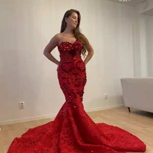 Röd klänning - Helt ny, oanvänd, fantastisk röd långklänning med paljetter och broderade detaljer. Klänningen är axelbandslös och har en tight passform som framhäver figuren. Perfekt för en glamorös kväll. Går att testa klänningen innan köp i Göteborg. 