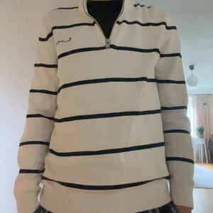 Vit randig half zip tröja från Bondelid - Snygg vit tröja från Bondelid med mörkblå horisontella ränder och half zip-dragkedja vid halsen. Tröjan har lång ärm, ribbade muddar och broderad logga på bröstet. Perfekt för dig som gillar klassisk och fräsch stil. Tröjan har inga synliga defekter, knappt använd ser ny ut. tröjan äe S men passar även M