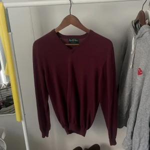 Vinröd merinoullströja Alan Paine - Vinröd långärmad tröja från Alan Paine i 100% merinoull. Klassisk v-ringad modell med ribbade muddar och en mjuk, tunn känsla.