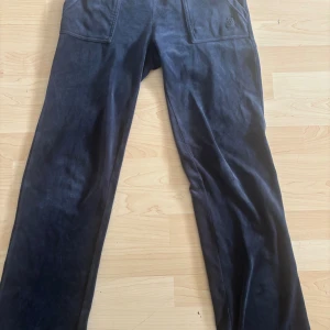 Juicy Couture mörkblå mjukisbyxor XS - Mörkblå mjukisbyxor från Juicy Couture i supermjuk velour. Byxorna har raka ben, stora fickor fram och bak med knappdetaljer och broderad logga på ena fickan. Perfekta för en chill och trendig look.