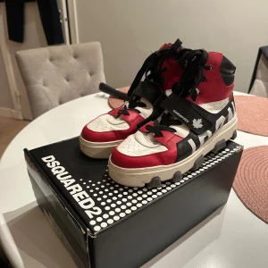 Dsquared2 Basket Icon sneakers röd/vit/svart - Säljer ett par Dsquared2 Basket Icon sneakers i rött, vitt och svart skinn. Höga sneakers med kraftig sula där det står 'ICON' undertill, snörning och kardborreband med Dsquared2-logga. Riktigt statement-skor för dig som vill sticka ut. Nypris: 5999kr