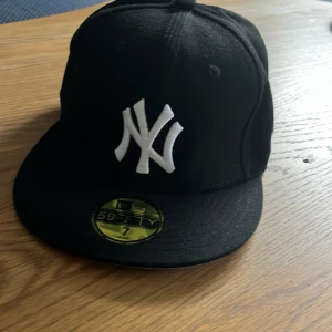 Svart New Era Yankees keps  - Klassisk svart New Era 59FIFTY keps med New York Yankees-logga broderad i vitt framtill och MLB-logga bak. Rak skärm och tight passform, tillverkad i bomull. Helt oanvänd då den var för liten. 