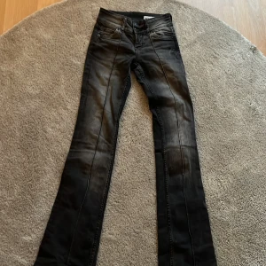 Svarta low waist  bootcut jeans från Bershka - Snygga svarta jeans från Bershka i bootcut-modell med lätt tvättad look. Klassisk femficksdesign, dubbla knappar i midjan och raka ben som släpper ut nedtill. Perfekta för dig som gillar en stilren men edgy vibe.