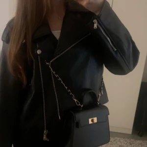 Svart skinnjacka från NA-KD - Snygg svart bikerjacka från NA-KD i imitationsskinn. Storlek S. Jackan är i mycket bra skick och endast använd ett fåtal gånger. Har dragkedjor och silverdetaljer för en trendig look. Passar perfekt till både vardag och fest.