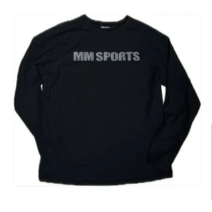 Svart långärmad tröja MM Sports - Svart långärmad tröja från MM Sports med tryckt logga i grått över bröstet. Tröjan har rund halsringning och är tillverkad i ett mjukt bomullsmaterial, perfekt för träning eller chill. Enkel och stilren design som funkar till det mesta.