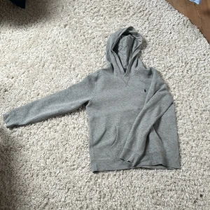 Grå hoodie från Polo Ralph Lauren - Klassisk grå hoodie från Polo Ralph Lauren med liten broderad logga på bröstet. Tröjan har huva, känguruficka och långa ärmar. Tillverkad i mjuk bomullsmix som är perfekt för kyligare dagar. Storlek XL 18-20 men kommer passa upp till S. Priset är inte hugget i sten. Den är i jätte fint skick med inga hål eller fläckar.