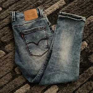 Levis jeans i blå denim - Snygga Levis jeans i blå denim med klassisk femficksdesign och en läderpatch baktill. De har en straight passform och är perfekta för en avslappnad stil. Midjan är midwaist och de har en dragkedja framtill.