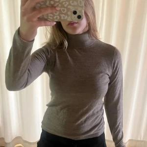 Brun polotröja i ull från Newhouse - Säljer en brun polotröja från Newhouse i 100% ull. Tröjan har lång ärm, klassisk polokrage och en slim passform som sitter snyggt. Perfekt att styla med jeans eller kjol för en enkel och clean look.