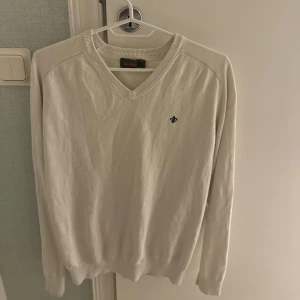 Vit v-ringad tröja från Morris - Vit v-ringad tröja från Morris med diskret broderad logga på bröstet. Tröjan har långa ärmar och ribbade muddar vid hals, ärmslut och nederkant. Perfekt för en clean och stilren look.