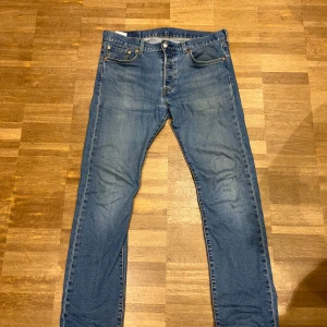 Levi's 501 blå jeans W30 L30 - Klassiska Levi's 501 jeans i blå denim med raka ben och femficksmodell. Jeansen har knappgylf och den ikoniska läderpatchen bak i midjan. Perfekt för dig som gillar tidlös stil och vill ha ett par riktigt schyssta jeans.