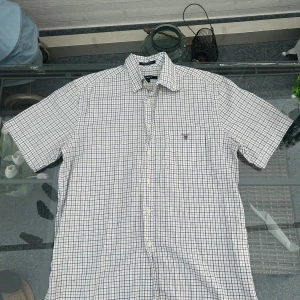 ✨ GANT rutig skjorta M Regular Fit ✨ - Klassisk och tidlös GANT-skjorta i rutigt mönster med beige, blå och vita toner. Storlek M och Regular Fit – sitter snyggt men avslappnat. Tillverkad i mjuk bomull som andas, perfekt både till vardags och mer uppklätt. Har en bröstficka med broderad GANT-logga och button-down-krage.  Passar lika bra till jeans som chinos, perfekt för dig som gillar preppy stil eller vill addera en stilren skjorta till garderoben.  Skick: Väldigt fint begagnat skick – inga fläckar eller hål.