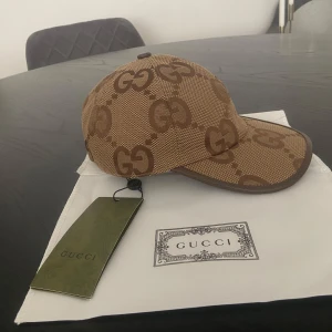 Beige Jumbo gucci keps  - Snygg keps från Gucci i beige och brunt med det klassiska GG-monogrammet över hela kepsen. Justerbar rem baktill och detaljer i canvas. Perfekt accessoar för att lyfta din outfit med lyxig känsla.