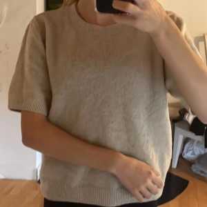 Beige stickad kortärmad tröja - Beige stickad tröja med korta ärmar och rund halsringning. Tröjan har en enkel och clean look med ribbade muddar vid ärmslut och hals. Perfekt för dig som är lite känslig mot tröjor som sticks.