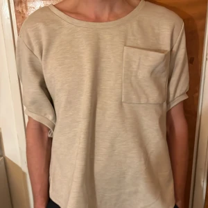 Beige loose topp med knytband - Snygg beige topp i loose fit med korta ärmar och stor bröstficka. 