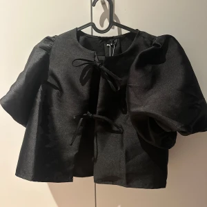 Svart puffärm blus med knyt - Svart blus med stora puffärmar och två knyt framtill. Oanvänd med lapp kvar, från Gina Tricot. 
