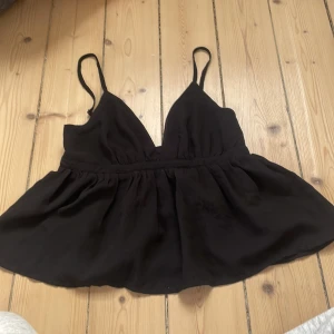 Svart linnetopp från Bik Bok XS - Supersöt svart linnetopp från Bik Bok i storlek XS. Toppen har smala axelband, v-ringning och en lätt utställd, flowy nederdel. Tillverkad i ett mjukt tyg med dragkedja i sidan för enkel påklädning. Perfekt för dig som gillar en enkel men stilren look.