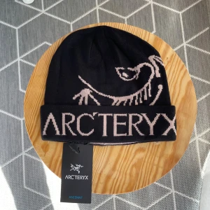Arc’teryx Ascent Beanie – Svart – Aldrig använt! - Svart mössa från Arc'teryx med ljusrosa logga och ikoniskt fossilmotiv. Stickad i mjukt material med uppvikt kant där Arc'teryx står tydligt. Perfekt för kalla dagar och snygg till streetwear eller outdoor-stil.