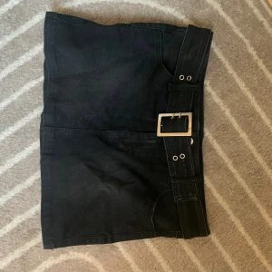 Svart jeanskjol med bälte från ONLY - Svart kort jeanskjol från ONLY med bredt bälte och silverfärgat spänne. Denim med rak passform. Perfekt för dig som gillar en stilren och edgy look.