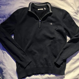 Mörkblå GANT half zip tröja - Snygg mörkblå tröja från GANT med halv dragkedja och ribbad krage med vita ränder. Liten broderad logga på bröstet och långa ärmar. Perfekt för dig som gillar klassisk och stilren look.