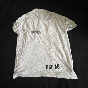 Vit t-shirt med graffiti-tryck XL - Vit t-shirt från 157 i 100% bomull med svart graffiti-inspirerat tryck på bröstet och ryggen samt texten 'RGO AB' framtill. Klassisk passform och korta ärmar, perfekt för en streetwear-look.