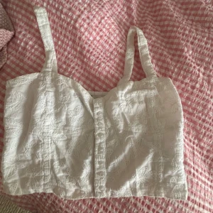 Vit broderad linnetopp med knappar - Superfin vit linnetopp från Bik Bok med broderade fjärilar och dekorativa knappar framtill. Toppen har breda axelband och är croppad, perfekt för varma dagar. Materialet är mjukt och luftigt bomull, vilket gör den skön att bära.