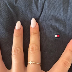 Mörkblå t-shirt från Tommy Hilfiger - Snygg mörkblå t-shirt från Tommy Hilfiger med klassisk rund hals och liten broderad logga på bröstet. Tillverkad i mjuk bomull som är skön att ha på sig. Perfekt basic-plagg med stilren design.