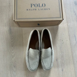   Ralph Lauren loafers - Snygga loafers från Polo Ralph Lauren i beige mocka. Klassisk och stilren design med rund tå och platt sula. Perfekta för dig som gillar en clean och tidlös look. Skorna är i storlek EU 44 och kommer i originalkartong. Kvitto finns! 