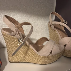 Beige wedge sandaler från Amisu - Snygga sandaler från Amisu i beige mockaimitation med höga flätade platåklackar i rep. Skorna har öppen tå, korsade remmar framtill och justerbart spänne vid ankeln. Perfekta för sommarens alla tillfällen när du vill ha lite extra höjd.