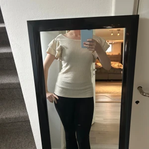 Beige ribbad topp med volangärm - Säljer en beige ribbad topp med korta volangärmar och rund halsringning. Toppen har en snygg, något djupare rygg och är figurnära i modellen. Perfekt för dig som gillar feminina detaljer och enkel stil.🩷