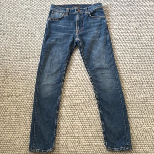 Nudie Jeans Lean Dean blå jeans - Säljer ett par Nudie Jeans Lean Dean i tvätten Troubled Sea. Klassiska blå jeans med orange sömmar, fem fickor och snygg broderad detalj på bakfickorna. Materialet är 99% bomull och 1% elastan för lite stretch. Perfekt passform med smalare ben.