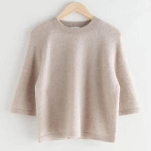 Beige stickad tröja med trekvartsärm - Supermjuk beige stickad tröja med rund hals och trekvartsärmar. Tröjan har en avslappnad passform och är perfekt för lager-på-lager under kyliga dagar. Enkel och stilren design som funkar till det mesta.