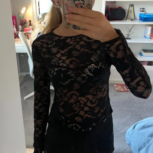Svart spetsblus från H&M - Säljer en svart långärmad blus från H&M i genombruten spets med blommigt mönster. Toppen har rund halsringning och är figurnära med transparenta partier som ger en snygg look. Perfekt att styla med jeans eller kjol.