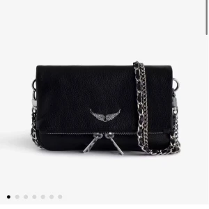 Svart axelväska från Zadig & Voltaire - Snygg svart axelväska i skinn från Zadig & Voltaire med silverfärgade kedjor och dragkedjor.  Köptes för några år sedan men är sparsamt använd, därav det fina skicket. Skriv om ni vill ha bilder. Heter nano rock clutch (lilla modellen) Nypris ca 2500 kr. 