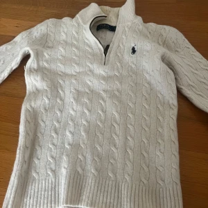 Vit kabelstickad tröja Polo Ralph Lauren - Vit kabelstickad tröja från Polo Ralph Lauren med half-zip. Litet hål som ni ser man går att sy ihop enkelt. Size S. Ja noppar den innan ja skickar! 