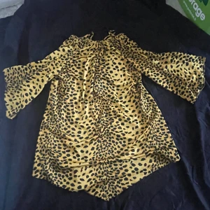 Leopardmönstrad klänning Moneta - Cool leopardmönstrad klänning från Moneta of Sweden i storlek 40. Klänningen har trumpetärmar, resår vid halsen och är i en gul och svart färgkombination. Perfekt för dig som vill sticka ut med ett djurmönster och en avslappnad passform.