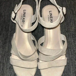 Klack - Snygga beige sandaler från Linear of Sweden med flera remmar och justerbart spänne vid ankeln. Skorna har en trendig kilklack i repimitation och ovandel i mockaliknande material. Perfekta för varma dagar och ger en somrig vibe till din outfit.Använda en gång 