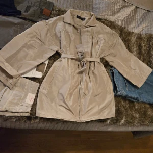 Beige trenchcoat - Stilren beige trenchcoat från Zara Woman med knytskärp i midjan och dragkedja framtill. Jackan har trekvartsärmar och klassisk krage. Osäker om den har använts eller inte men inga skador iallafall på den.