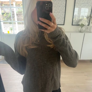 Brun/beige stickad tröja med lång ärm - Mysig brun/beige stickad tröja med lång ärm och rund hals. Tröjan har en rak passform och ribbade muddar vid ärmslut och nederkant. Även en detalj på framsidan av tröjan! 💕