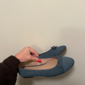 Blå ballerinaskor i jeansmaterial - Snygga blå ballerinaskor i jeansmaterial med rund tå och liten rosett framtill. Skorna har platt sula och en klassisk, enkel design som passar perfekt till både jeans och klänning. Perfekta för dig som gillar en stilren och avslappnad look.