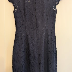 Mörkblå spetsklänning från H&M - Mörkblå kort klänning från H&M i spets med blommigt mönster. Klänningen har korta ärmar, figurnära passform och öppen rygg. Perfekt för dig som gillar eleganta detaljer och vill sticka ut med en klassisk look.
