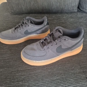 Nike Air Force 1 med gummisula - Säljer ett par svarta Nike Air Force 1 med klassisk gummifärgad sula. Skorna har snörning och är tillverkade i textil och syntetmaterial. Perfekta för dig som gillar stilrena sneakers med en twist. Swoosh-loggan på sidan och låg profil.