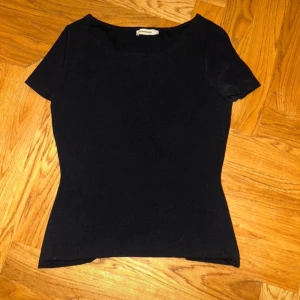 Svart omlottopp från Andiata - Säljer en svart omlottopp från J. Lindeberg med korta ärmar och rund halsringning. Toppen har en snygg omlottdetalj baktill som ger en unik look. Tillverkad i mjuk bomull med en tight passform som framhäver figuren.